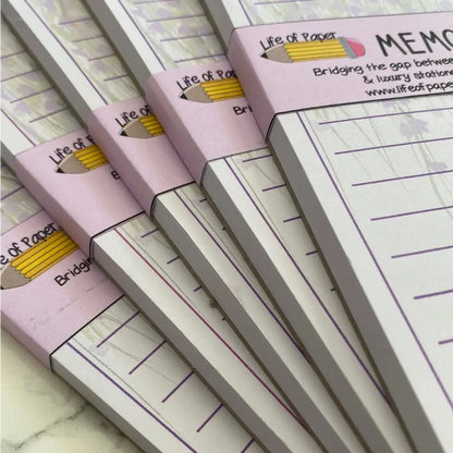 A close-up image of several stacked pastel-colored Wisteria Memo Pads with the branding "Life of Paper" at the top. The notepads, perfect for your shopping list or to-do list, feature a pencil icon and the phrase "Bridging the gap between simplicity & luxury stationery" on the cover.